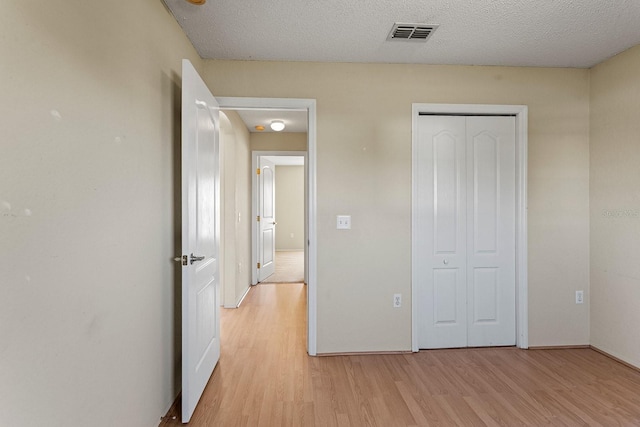 unfurnished bedroom with a textured ceiling, light hardwood / wood-style flooring, and a closet