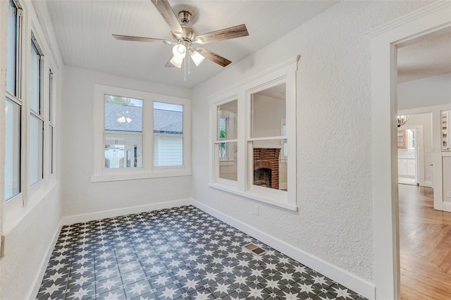 unfurnished sunroom with ceiling fan with notable chandelier and a brick fireplace