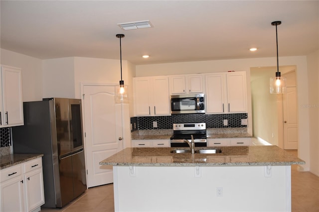 kitchen with dark stone countertops, pendant lighting, a center island with sink, white cabinets, and appliances with stainless steel finishes