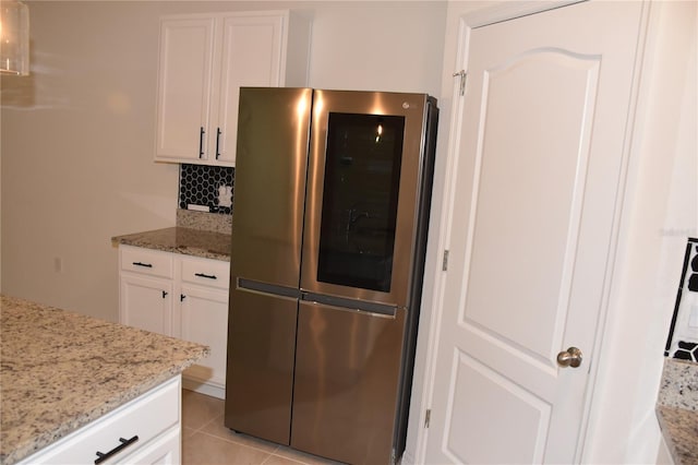 kitchen with decorative backsplash, stainless steel fridge, white cabinets, and light stone counters