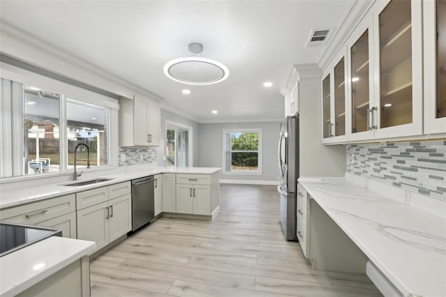 kitchen with backsplash, crown molding, sink, light stone countertops, and stainless steel appliances