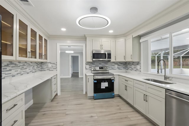 kitchen with light stone countertops, sink, stainless steel appliances, white cabinets, and ornamental molding