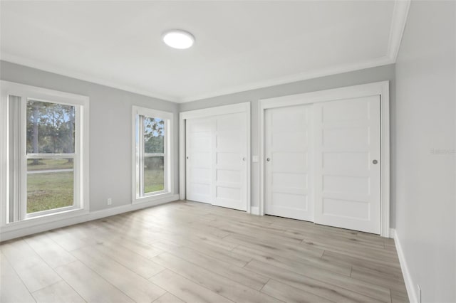 unfurnished bedroom with light wood-type flooring, crown molding, and multiple closets