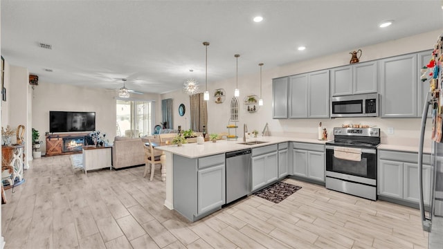 kitchen featuring ceiling fan, sink, hanging light fixtures, stainless steel appliances, and kitchen peninsula