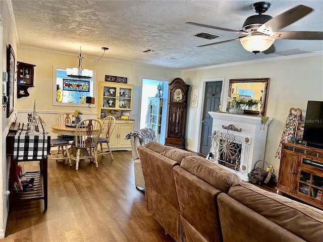 living room with hardwood / wood-style flooring, ceiling fan with notable chandelier, ornamental molding, and a textured ceiling