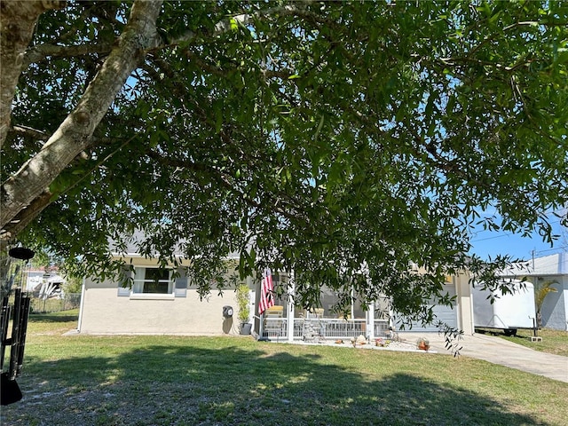 view of property hidden behind natural elements with a porch, a front yard, driveway, and fence