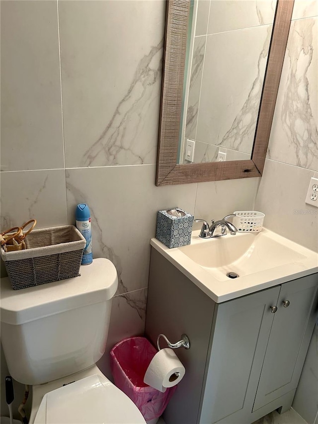 half bath featuring tile walls, toilet, and vanity
