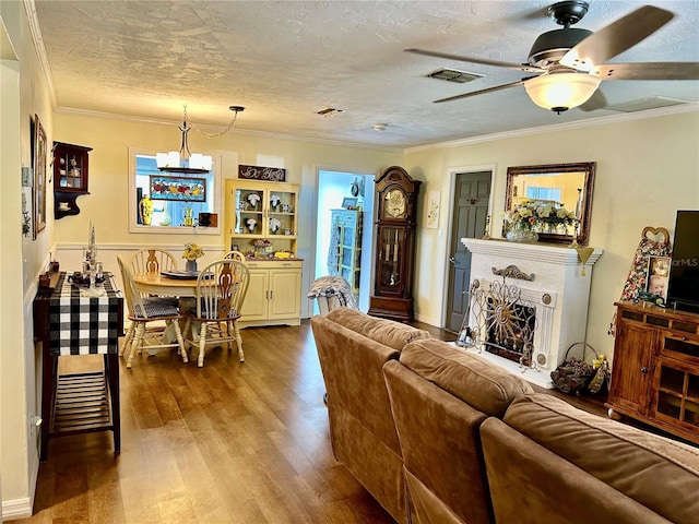living room with crown molding, a fireplace with raised hearth, a textured ceiling, visible vents, and wood finished floors