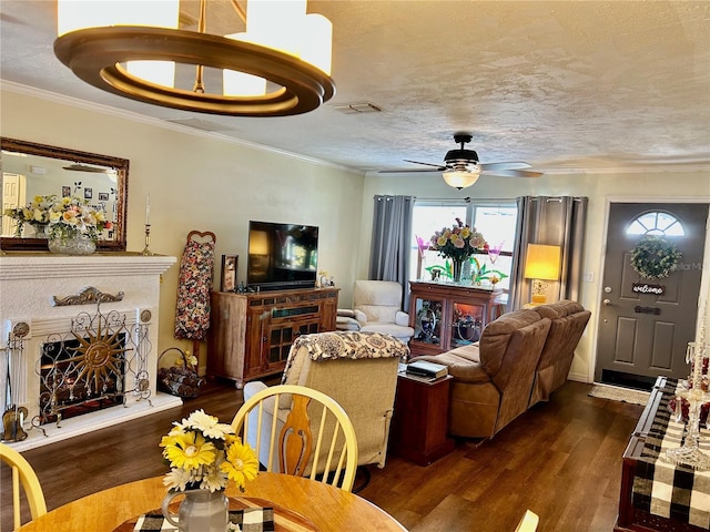 living room featuring dark wood-style flooring, ornamental molding, a textured ceiling, visible vents, and a ceiling fan