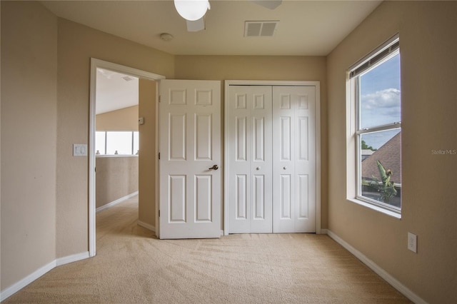 unfurnished bedroom with ceiling fan, a closet, light colored carpet, and multiple windows