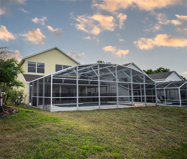 back house at dusk featuring glass enclosure and a lawn