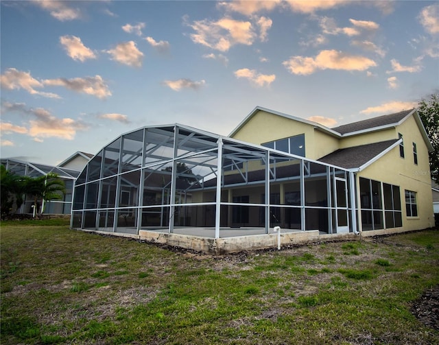 back house at dusk with glass enclosure and a yard