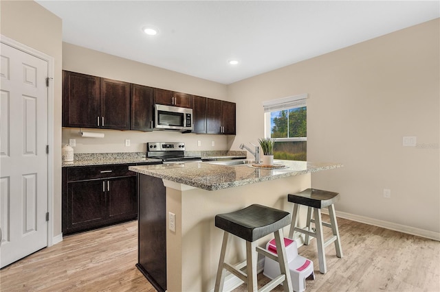 kitchen with light hardwood / wood-style floors, stainless steel appliances, a breakfast bar area, and an island with sink