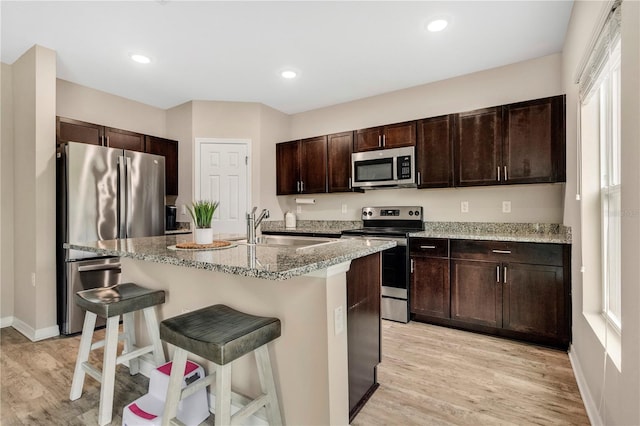 kitchen featuring sink, stainless steel appliances, a kitchen bar, dark brown cabinets, and a center island with sink