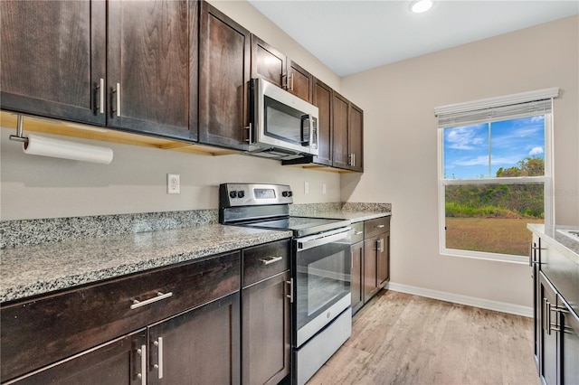 kitchen featuring appliances with stainless steel finishes, dark brown cabinetry, light hardwood / wood-style flooring, and light stone counters