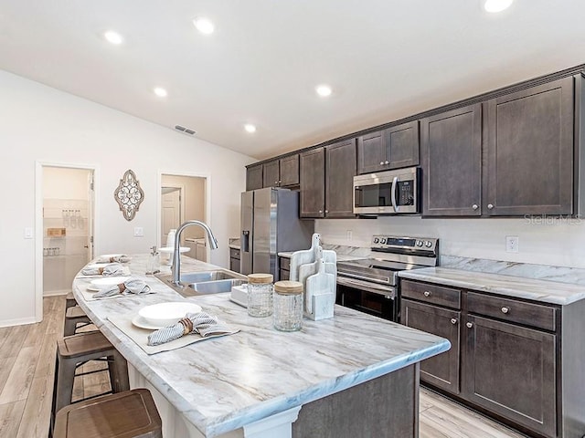 kitchen featuring sink, stainless steel appliances, an island with sink, light hardwood / wood-style floors, and a kitchen bar