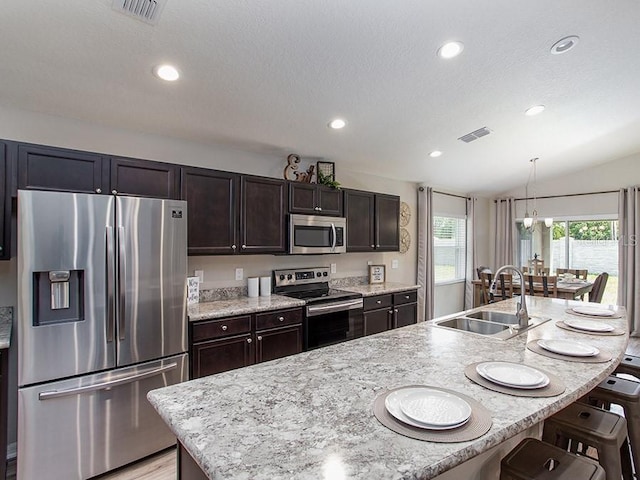 kitchen with sink, stainless steel appliances, an island with sink, vaulted ceiling, and a kitchen bar