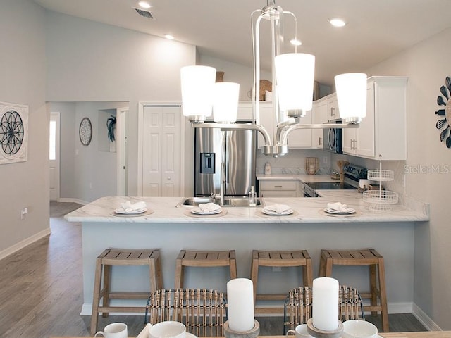 kitchen with kitchen peninsula, appliances with stainless steel finishes, light stone countertops, a breakfast bar, and white cabinets