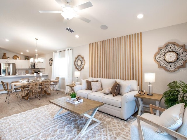 living room with lofted ceiling, light hardwood / wood-style flooring, and ceiling fan with notable chandelier