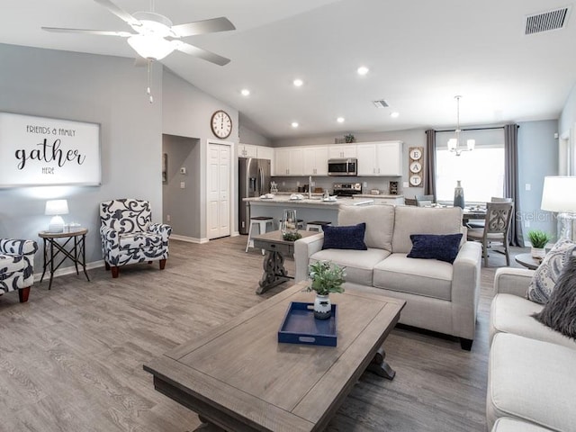 living room with ceiling fan with notable chandelier, hardwood / wood-style flooring, and vaulted ceiling