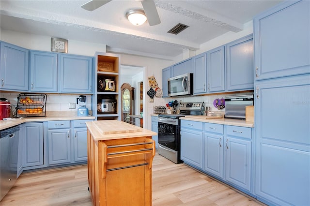 kitchen featuring appliances with stainless steel finishes, tasteful backsplash, blue cabinets, ceiling fan, and light hardwood / wood-style flooring