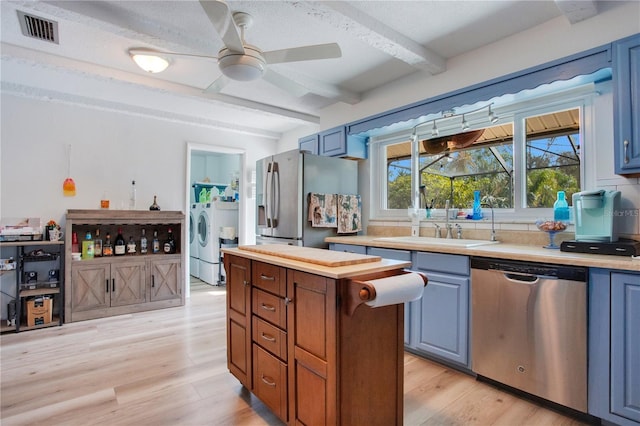 kitchen with appliances with stainless steel finishes, ceiling fan, light hardwood / wood-style flooring, beamed ceiling, and washer / clothes dryer