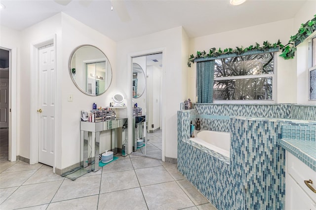 bathroom with tile patterned floors, ceiling fan, vanity, and tiled bath