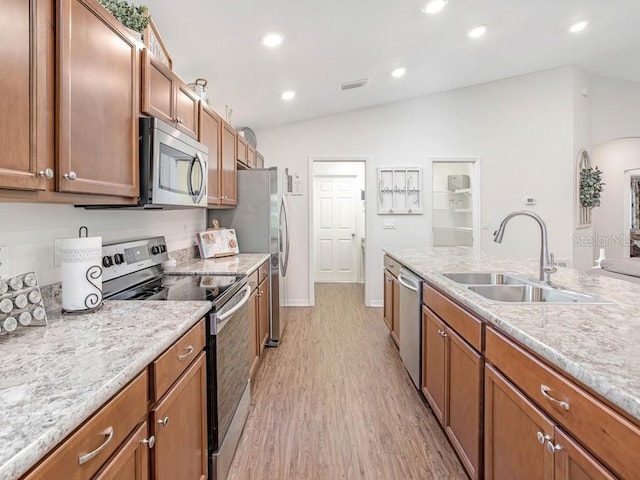 kitchen featuring lofted ceiling, sink, appliances with stainless steel finishes, light hardwood / wood-style floors, and light stone counters