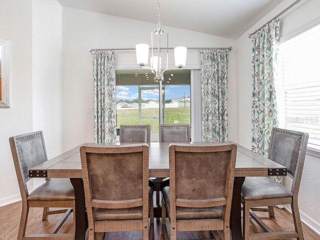 dining area with hardwood / wood-style floors, plenty of natural light, lofted ceiling, and an inviting chandelier