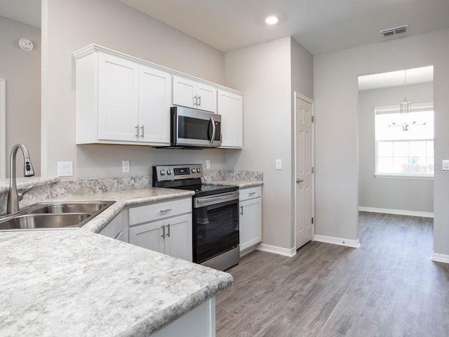 kitchen with appliances with stainless steel finishes, sink, white cabinets, light hardwood / wood-style floors, and hanging light fixtures