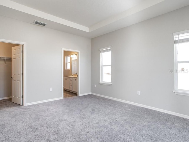 unfurnished bedroom with carpet flooring, ensuite bathroom, a tray ceiling, a spacious closet, and a closet