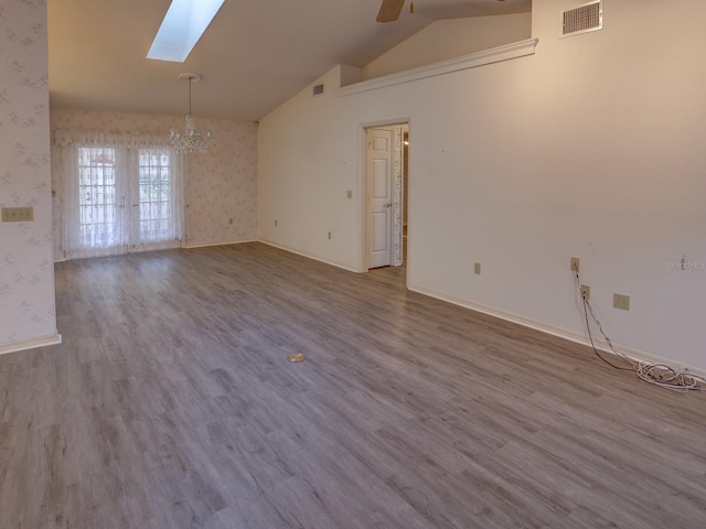 spare room with vaulted ceiling with skylight, ceiling fan with notable chandelier, and hardwood / wood-style floors