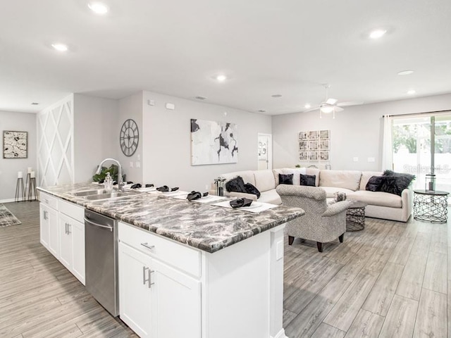 kitchen with light stone counters, sink, dishwasher, white cabinetry, and an island with sink