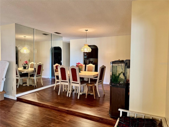 dining room featuring a textured ceiling, arched walkways, wood finished floors, and baseboards