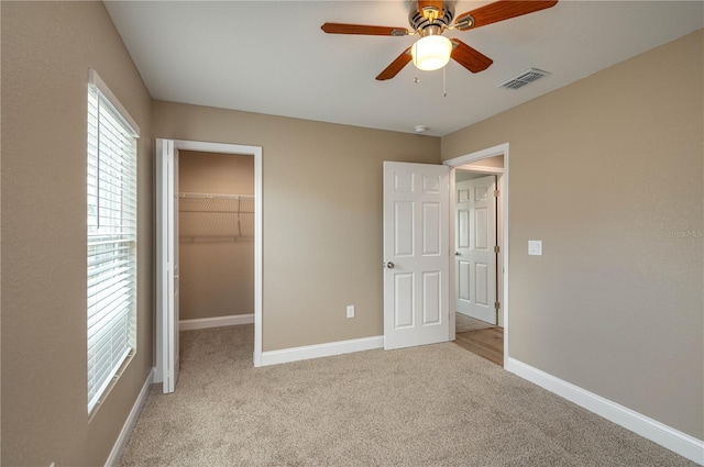 unfurnished bedroom featuring a spacious closet, a closet, ceiling fan, and light colored carpet