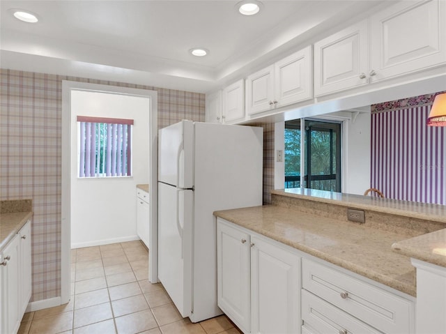 kitchen featuring white cabinets, white refrigerator, light stone countertops, a wealth of natural light, and light tile patterned flooring