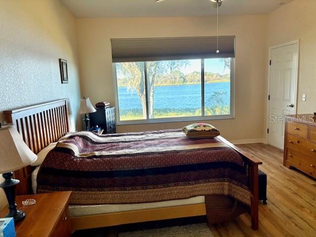 bedroom with multiple windows, light hardwood / wood-style flooring, and a water view