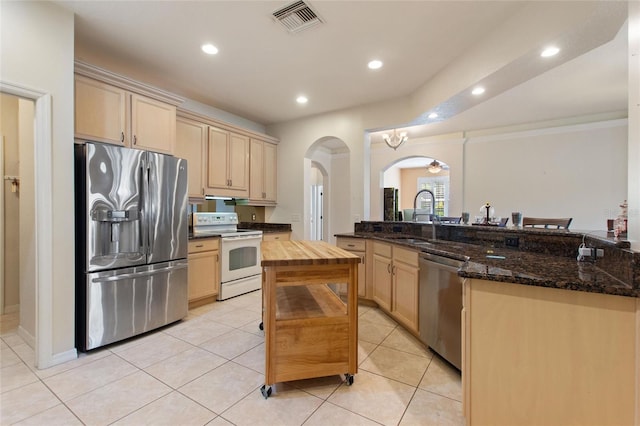 kitchen featuring appliances with stainless steel finishes, light brown cabinetry, sink, dark stone counters, and a center island