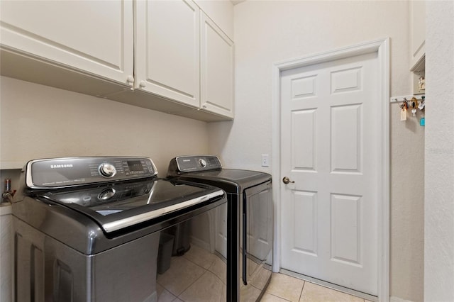 clothes washing area with washer and dryer, light tile patterned floors, and cabinets