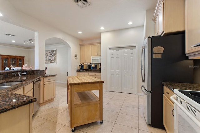 kitchen with dark stone counters, white appliances, light brown cabinetry, and light tile patterned floors