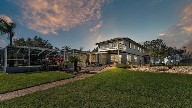 back house at dusk featuring a lanai and a yard