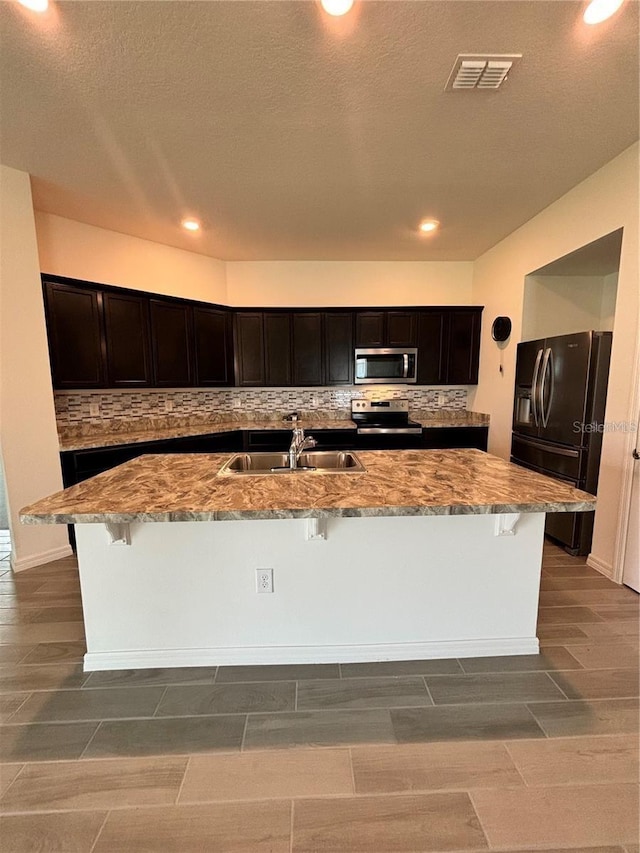 kitchen featuring sink, tasteful backsplash, a kitchen bar, a kitchen island with sink, and appliances with stainless steel finishes