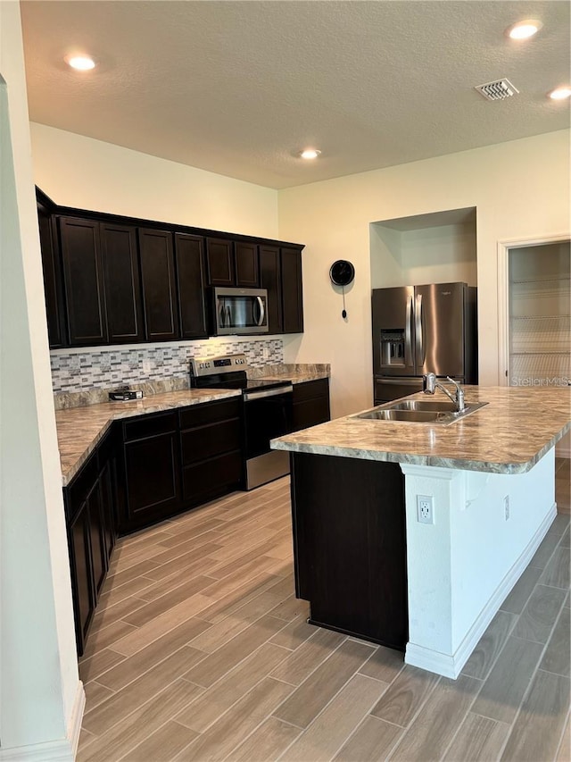 kitchen with a center island with sink, sink, appliances with stainless steel finishes, and tasteful backsplash