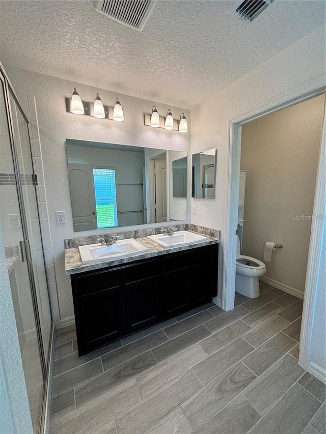 bathroom with vanity, toilet, an enclosed shower, and a textured ceiling