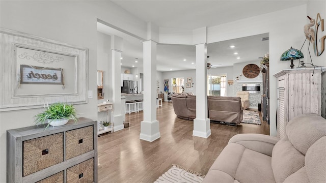 living room featuring decorative columns, ceiling fan, a fireplace, and hardwood / wood-style flooring