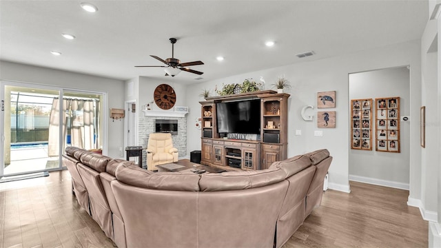 living room with ceiling fan, light hardwood / wood-style flooring, and a brick fireplace