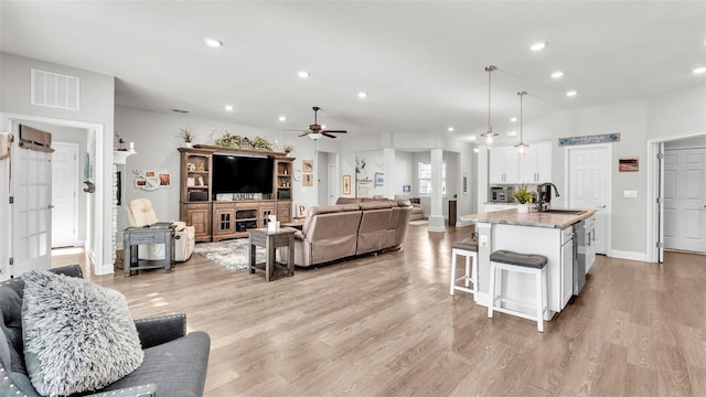 living room featuring ceiling fan, sink, a fireplace, and light hardwood / wood-style flooring