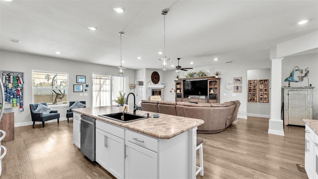 kitchen featuring stainless steel dishwasher, sink, pendant lighting, a center island with sink, and white cabinetry