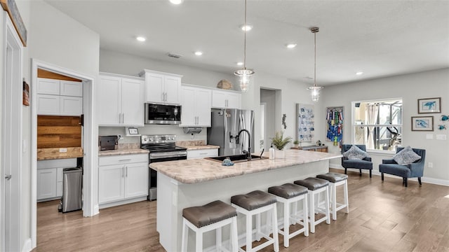 kitchen with stainless steel appliances, an island with sink, pendant lighting, a breakfast bar area, and white cabinets