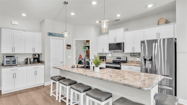 kitchen with a kitchen island with sink, white cabinetry, pendant lighting, and appliances with stainless steel finishes